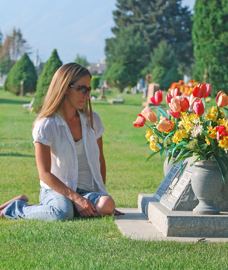 Woman Sitting Near Headstone In Cemetery